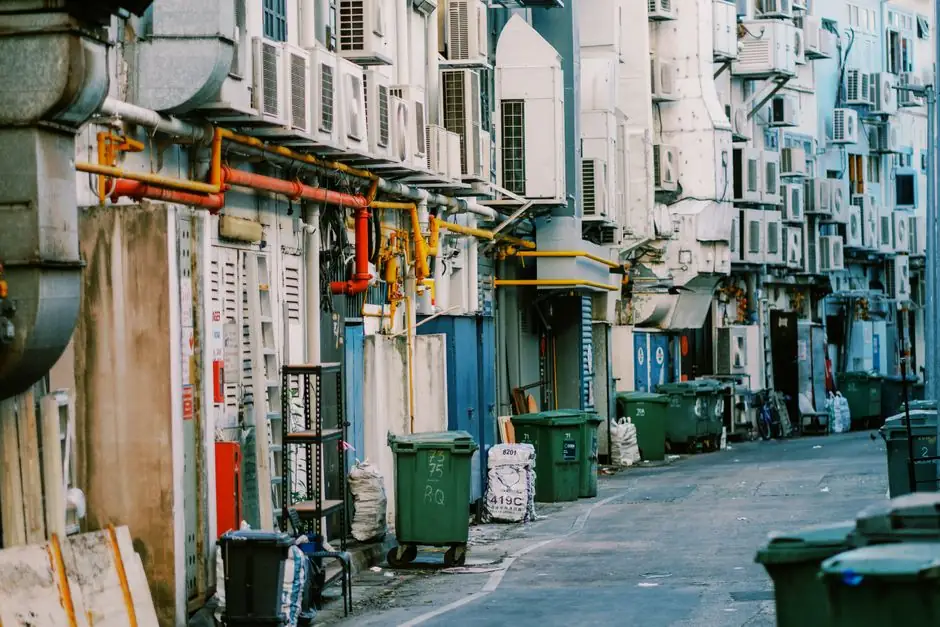 A narrow urban alley lined with numerous air conditioning units and trash bins.